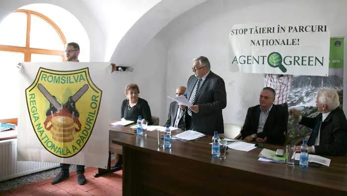 Partecipanti a un incontro accanto all’emblema di Romsilva e allo striscione di Agent Green “Stop ai tagli nei parchi nazionali!”