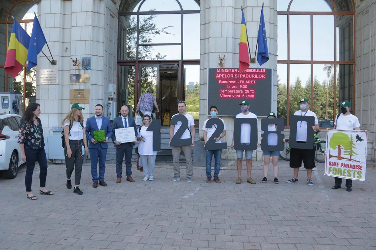 Un gruppo di persone con cartelli e cifre davanti a un edificio con bandiere.