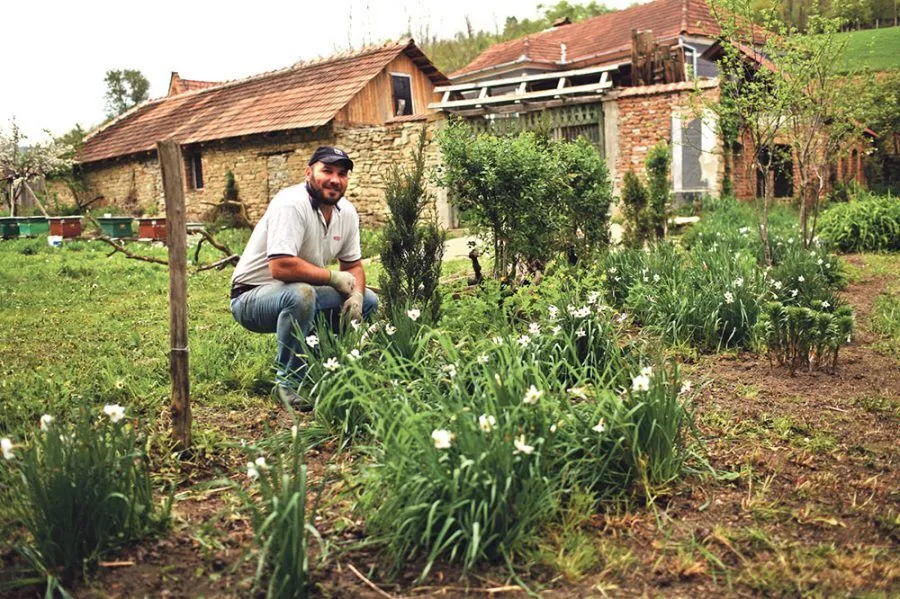 Ein Mann neben Blumen in einem Garten vor einem Haus.