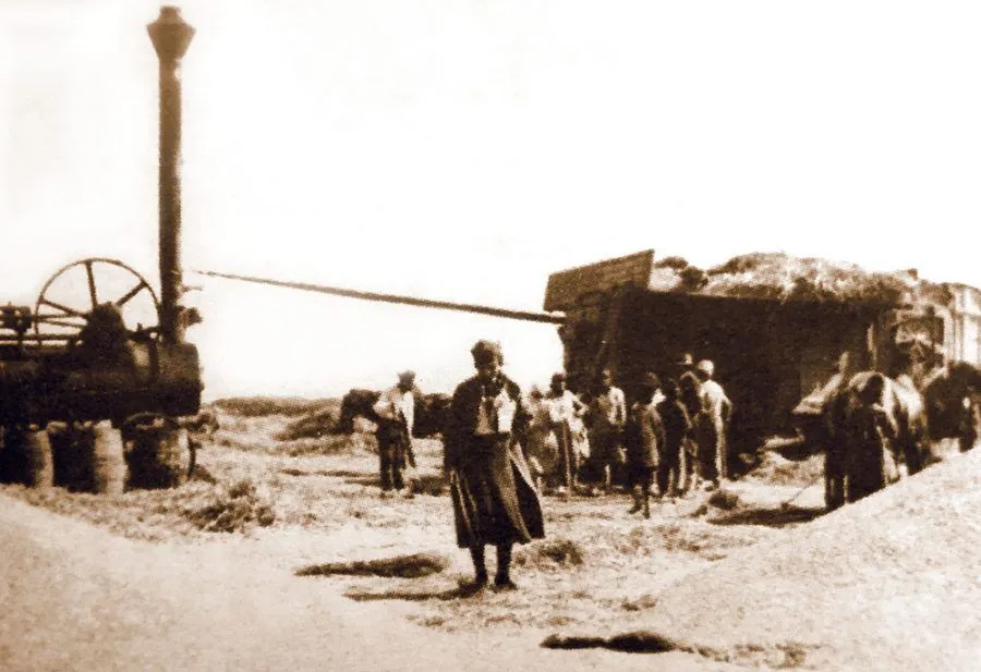 Historische Fotografie von Menschen neben Maschinen und Strohhaufen.