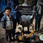 Un bambino con una bicicletta vicino a persone con un cartello sulla protezione degli animali selvatici.