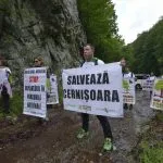 People with signs to save Cernișoara, beside a rocky slope.