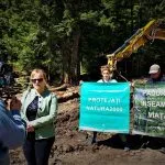 Persone con cartelli per proteggere la natura vicino a un macchinario forestale.