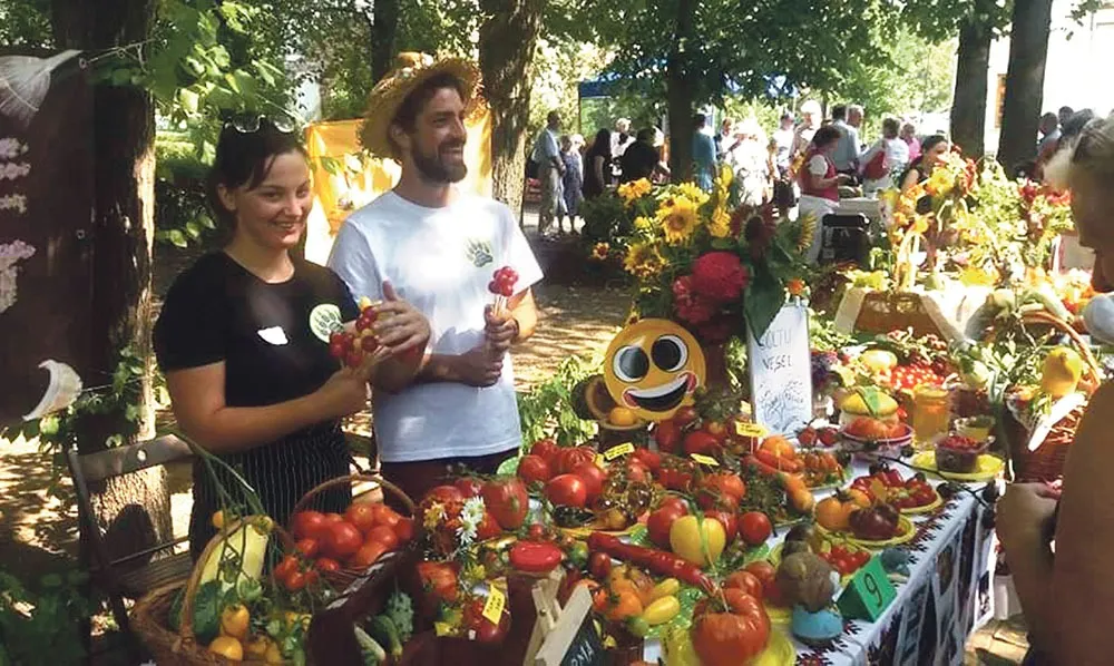 Teilnehmer an einem Gemüse- und Saatgutmarkt neben einem Tisch mit Erzeugnissen.
