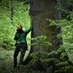 Una persona accanto al tronco di un albero di grandi dimensioni.