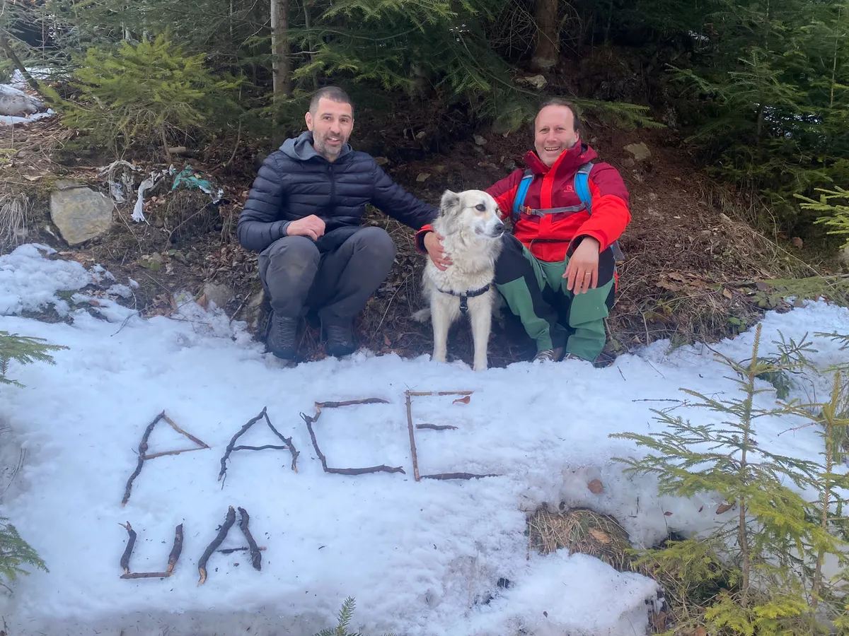 Due uomini e un cane in una foresta, accanto alla parola «PACE» scritta sulla neve.