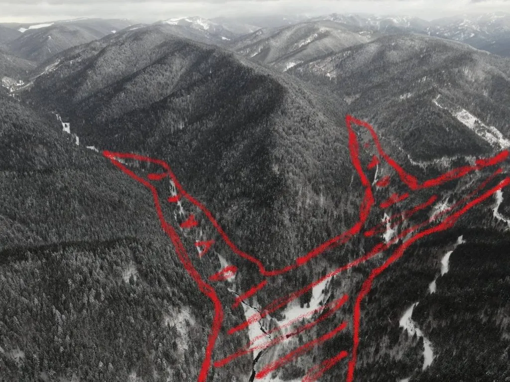 Veduta aerea di una valle boscosa con tracciati segnati in rosso.