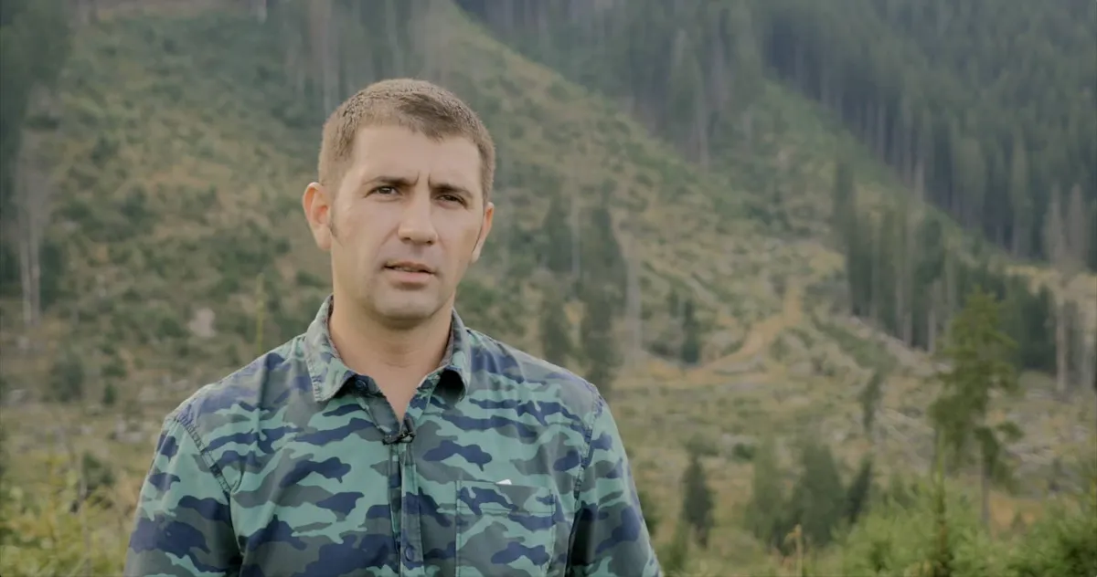 Man in a camouflage shirt, in front of a hillside with trees and open areas