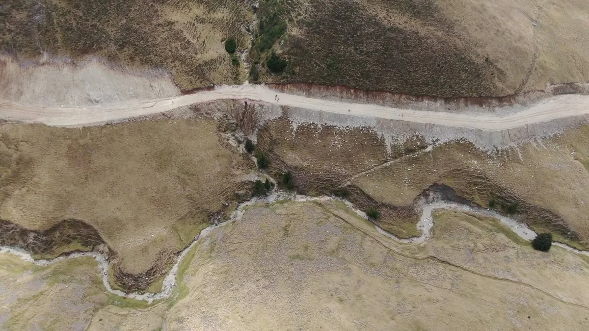 Blick von oben auf ein Gebirgsgelände mit einer Straße und einem Wasserlauf.