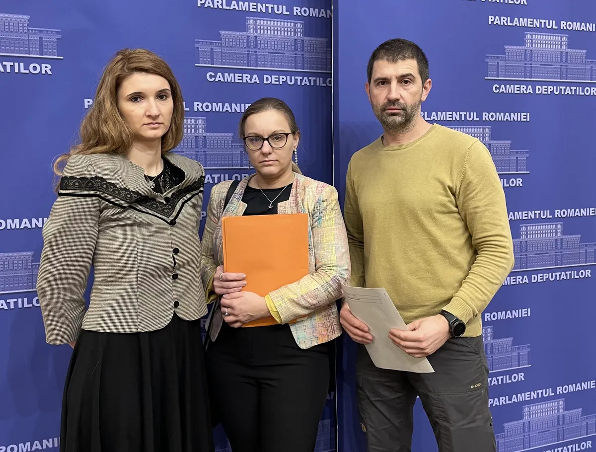 Three people in front of a Romanian Parliament sign, holding documents.